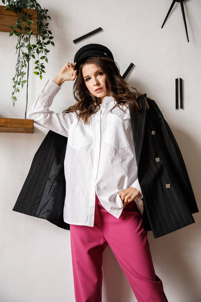 Fashion portrait of beauty brunette model wearing black jacket, white shirt and pink pants. Young beautiful woman posing in luxury apartments interior - Фото, изображение