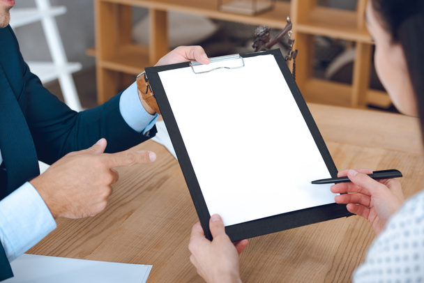 обрезанный снимок адвоката, указывающего на планшет и женщину, подписывающую бумаги
 - Фото, изображение