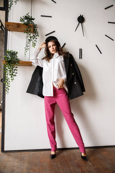 Fashion portrait of beauty brunette model wearing black jacket, white shirt and pink pants. Young beautiful woman posing in luxury apartments interior - Φωτογραφία, εικόνα