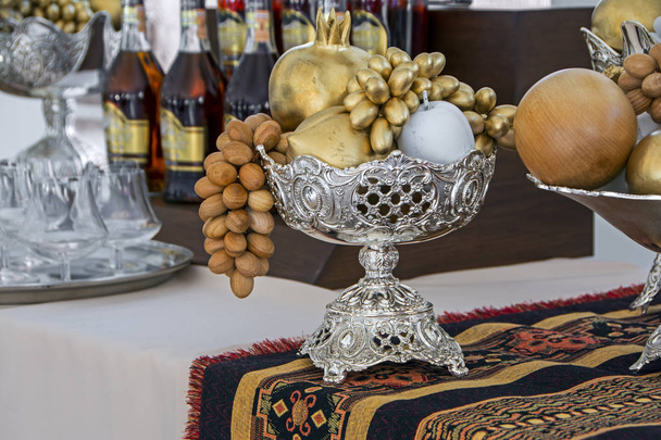 Dekorációs fa gyümölcs, hagyományos ezüst váza a örmény szőnyegeket az üveg alkohol és wineglasses, elmosódott háttér - Fotó, kép