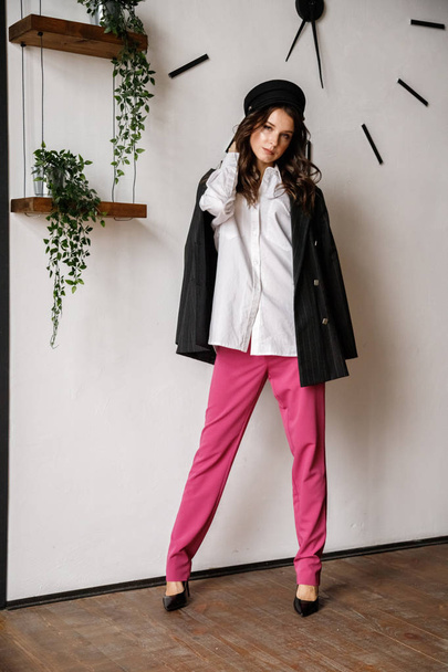 Fashion portrait of beauty brunette model wearing black jacket, white shirt and pink pants. Young beautiful woman posing in luxury apartments interior - Φωτογραφία, εικόνα