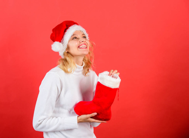 Christmas stocking concept. Girl cheerful face got gift in christmas sock. Check contents of christmas stocking. Traditional winter holiday. Woman in santa hat hold christmas gift red background - Φωτογραφία, εικόνα