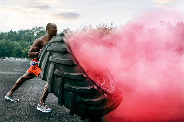 Handsome muscular man flipping big tire outdoor. - Photo, image