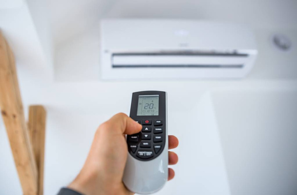 Man adjusting and regulating temperature on home air conditioner with remote control - Photo, Image