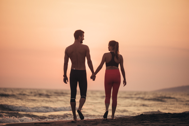Young man and woman in love walking hand in hand on sandy beach in sunset. - Foto, imagen