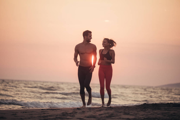 schöner kaukasischer Mann und schöne Frau laufen zusammen am Sandstrand im Sonnenuntergang. - Foto, Bild