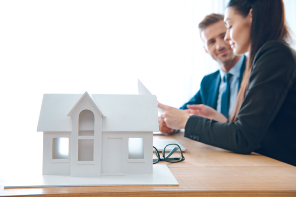 vue latérale des agents d'assurance sur le lieu de travail avec modèle de maison en papier dans le bureau, concept d'assurance maison
 - Photo, image