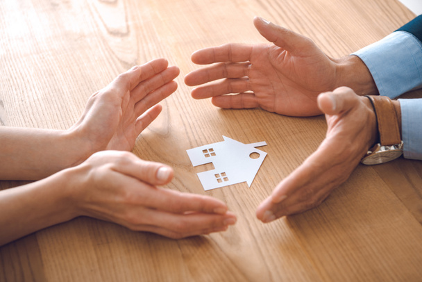 osittainen näkymä vakuutusasiamiesten ja naisten kädet paperi talon malli puinen pöytälevy, talon vakuutus käsite
 - Valokuva, kuva