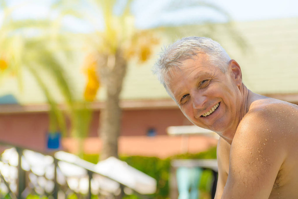 Przystojny mężczyzna na wakacjach, uśmiechając się do kamery, relaksując się przy basenie w Luxury Resort. Happy dojrzały człowiek korzystających lato wakacje w tropikalnym spa hotel. - Zdjęcie, obraz