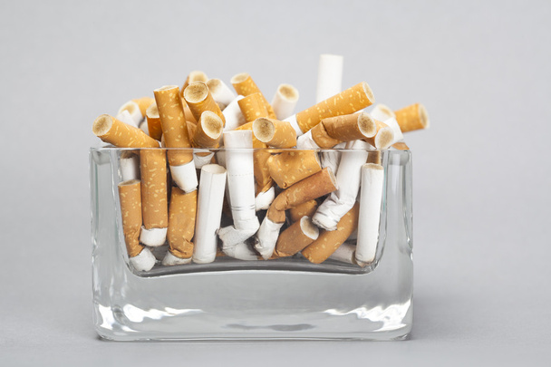 Попільничка повна сигарет на сірому фоні
 - Фото, зображення