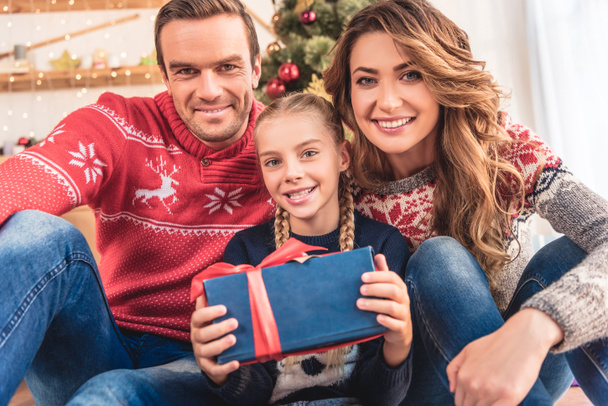 smiling parents and daughter with christmas present looking at camera at home - Photo, Image