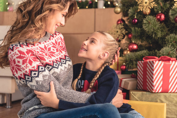 mother and daughter hugging near christmas tree and looking at each other at home - Photo, Image