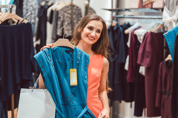 Γυναίκα ΣΚΕΨΕΙΣ αγοράζοντας ένα μπλε φόρεμα μόδας κατάστημα - Φωτογραφία, εικόνα