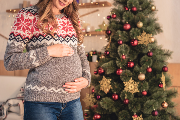 cropped image of pregnant woman in santa hat touching belly at home - Foto, Imagem