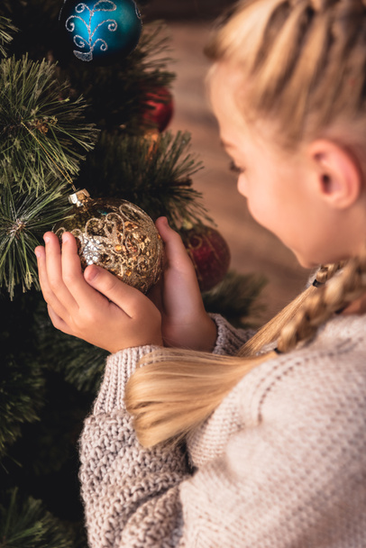 Selektiver Fokus eines entzückenden Frühchens, das zu Hause eine goldene Christbaumkugel in den Händen hält - Foto, Bild