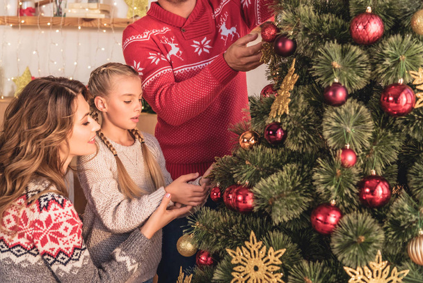 familia con hija decorando árbol de navidad con bolas en casa
 - Foto, imagen
