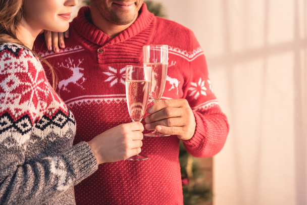 cropped view of couple in christmas sweaters holding glasses with champagne - Foto, afbeelding