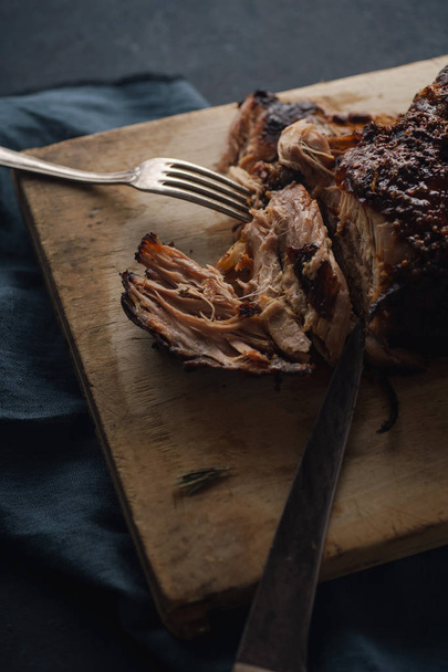 langsam gekochtes Schweinefleisch mit Zuckerglasur und Gabel mit Messer auf Holzschneidebrett, Nahaufnahme  - Foto, Bild