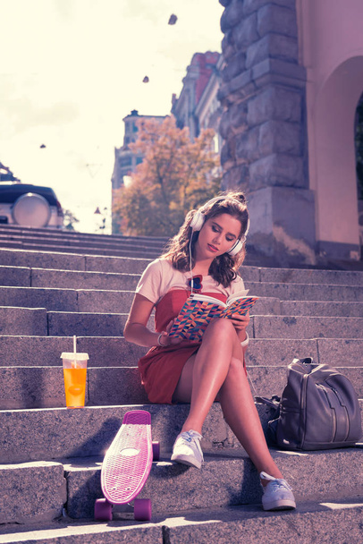 Young student girl sitting and reading book while waiting for her boyfriend - Фото, изображение