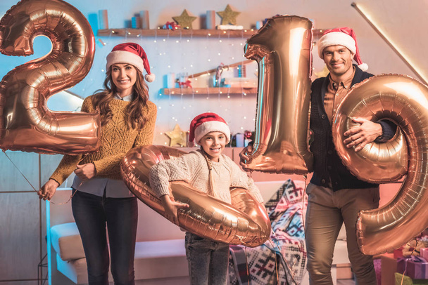 genitori felici con la figlia in cappelli di Babbo Natale che tengono 2019 nuovi palloncini d'oro anno
  - Foto, immagini