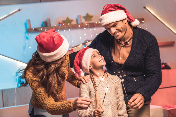heureux parents et fille dans chapeaux Santa célébrer Noël avec des étincelles
 - Photo, image