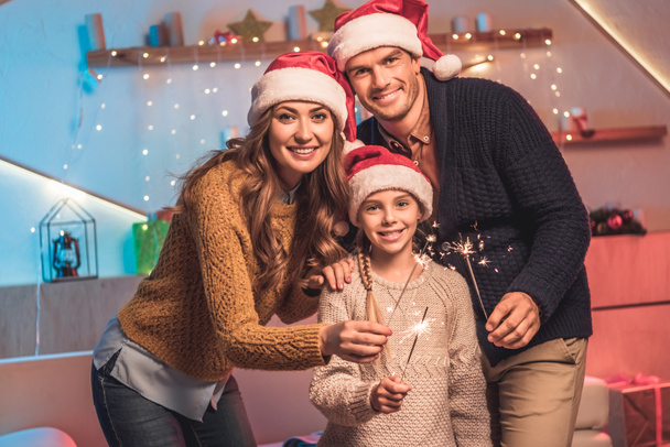 smiling family in santa hats celebrating new year with sparklers - Zdjęcie, obraz