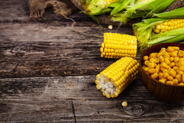 Ripe corn on an old wooden table. Raw corn and canned corn in a wooden bowl. - Photo, Image