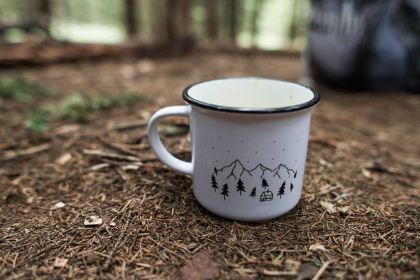 A vintage enamel tea or coffee mug sits on a tree stump in an outdoor setting. - Фото, зображення