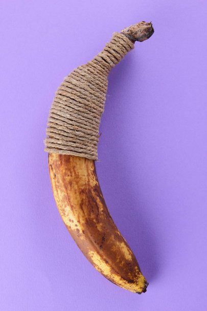 Blackened banana tied with twine. Banana on purple background. Spoiled tropical fruit in pop art style. Fruit concept. Source of food poisoning - Fotoğraf, Görsel