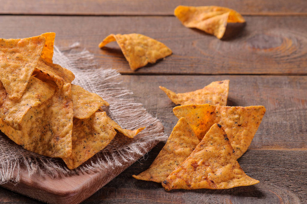 Chips. Een heleboel nachos op het bord op een bruin houten tafel. ongezonde voeding - Foto, afbeelding