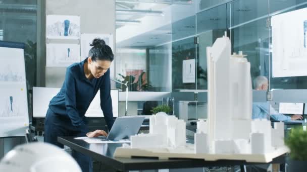 Kadın mimari Tasarımcısı, yeni bina modeli için kentsel tasarım projesi mühendislik bir dizüstü bilgisayarda çalışır. Temiz minimalist Office, beton duvarlar planları ve belgeler. - Video, Çekim