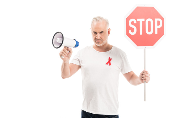 hombre maduro enojado en blanco camiseta blanca con la cinta roja del conocimiento del sida, señal de tráfico de la parada y megáfono aislados en blanco
 - Foto, imagen