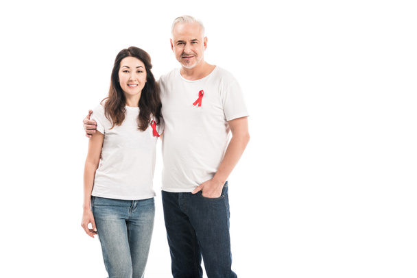 smiling adult interracial couple in blank t-shirts with aids awareness red ribbons embracing and looking at camera isolated on white - Photo, Image