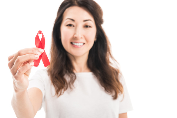 close-up portrait of happy adult asian woman holding aids awareness red ribbon isolated on white - Photo, Image