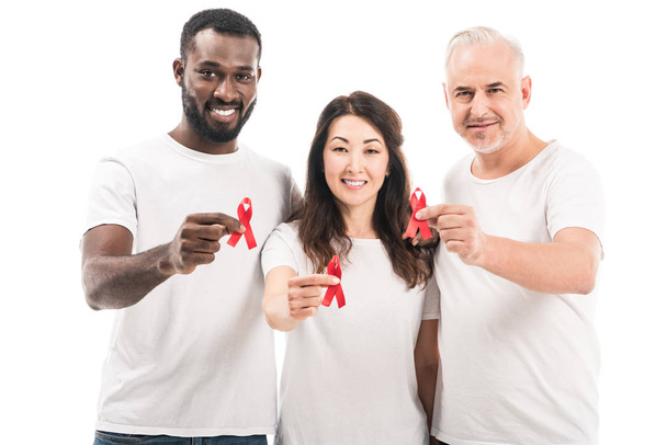 multiethnische Gruppe von Menschen in weißen T-Shirts mit Hilfsmitteln Bewusstsein roten Bändern und Blick in die Kamera isoliert auf weiß - Foto, Bild