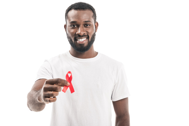 homme afro-américain souriant en t-shirt blanc vierge tenant aides à la sensibilisation ruban rouge et regardant la caméra isolée sur blanc
 - Photo, image