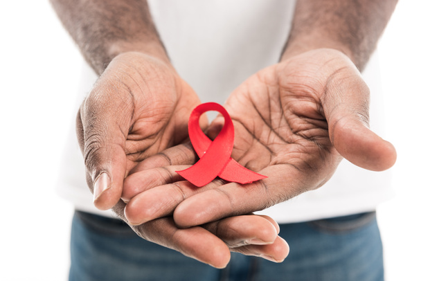 cropped shot of african american man holding aids awareness red ribbon isolated on white - Zdjęcie, obraz