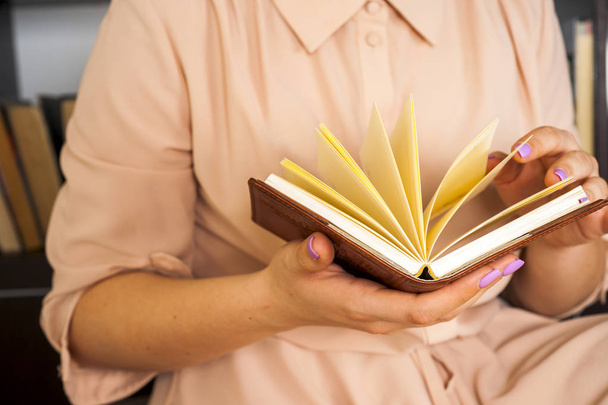 Ένα κορίτσι με ελαφρύ φόρεμα διαβάζει ένα βιβλίο. Τα γυναικεία χέρια κρατούν ένα βιβλίο στα χέρια τους. - Φωτογραφία, εικόνα
