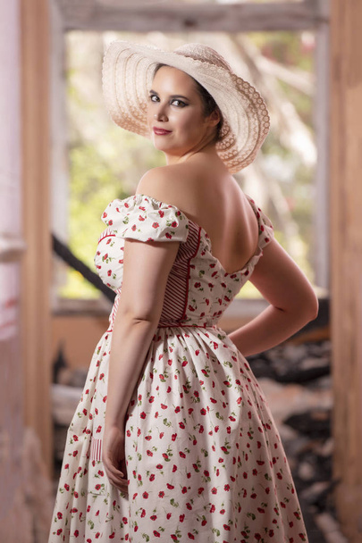 Vista de una joven dama contryside con vestido blanco y flores rojas y sombrero en un palacio abandonado
. - Foto, Imagen