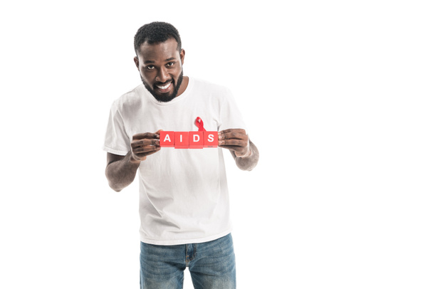 uomo afroamericano sorridente in bianco bianco t-shirt con aiuti consapevolezza nastro rosso e blocchi con scritta AIDS isolato su bianco
 - Foto, immagini