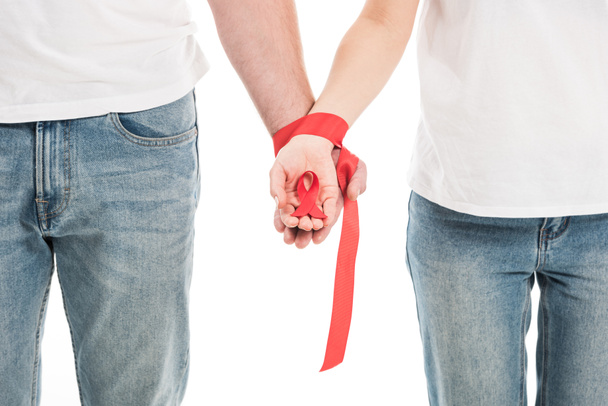 cropped shot of couple holding hands tied with red ribbon isolated on white, aids awareness day concept - Φωτογραφία, εικόνα