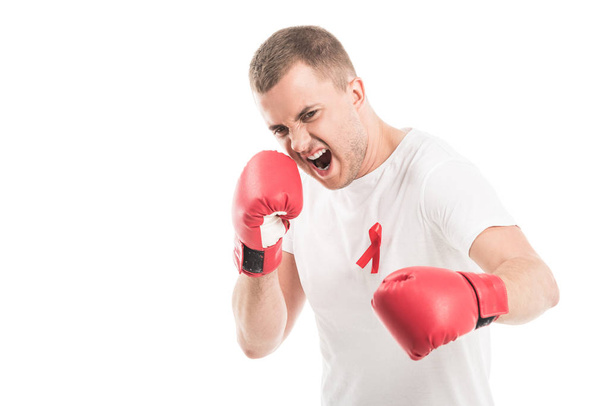angry handsome man in blank white t-shirt with aids awareness red ribbon and boxing gloves isolated on white, fighting aids concept - Foto, Imagen