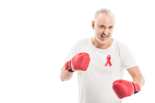 emotional mature man in blank white t-shirt with aids awareness red ribbon and boxing gloves isolated on white, fighting aids concept - Photo, Image