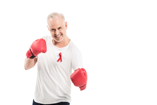 angry mature man in blank white t-shirt with aids awareness red ribbon and boxing gloves isolated on white, fighting aids concept - Photo, Image