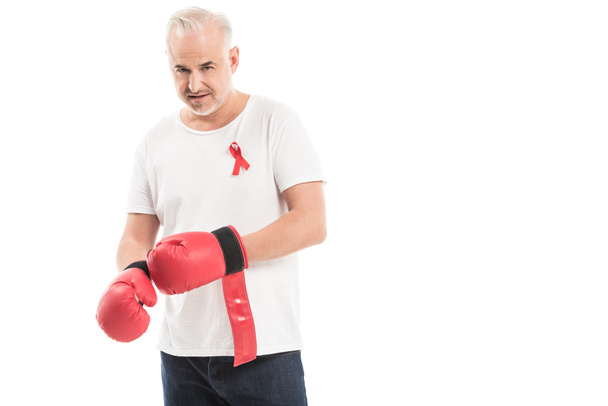 serious mature man in blank white t-shirt with aids awareness red ribbon and boxing gloves isolated on white, fighting aids concept - Fotoğraf, Görsel