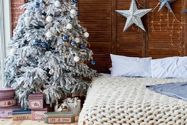 Christmas decorated bedroom interior with comfortable bed, Christmas fir tree and gift boxes on floor, copy space. Cozy home moment. Happy New Year. Christmas morning - Foto, Bild