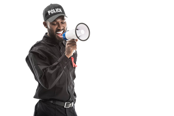 smiling african american police officer with aids awareness red ribbon shouting with megaphone isolated on white - Photo, Image