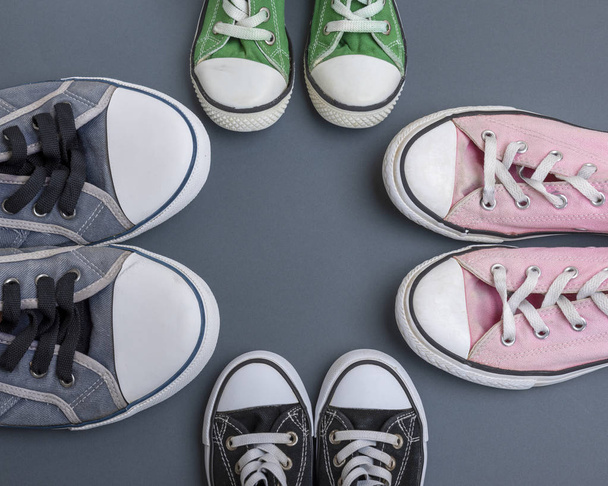 four pairs of old textile sneakers on a black background, women's, men's and children's shoes, copy space - Foto, Imagem