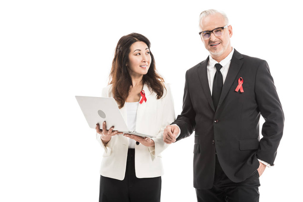 χαμογελώντας πολυεθνική ενηλίκων επιχειρηματίες με aids ευαισθητοποίησης κόκκινες κορδέλες λειτουργεί μαζί με το φορητό υπολογιστή που απομονώνονται σε λευκό - Φωτογραφία, εικόνα