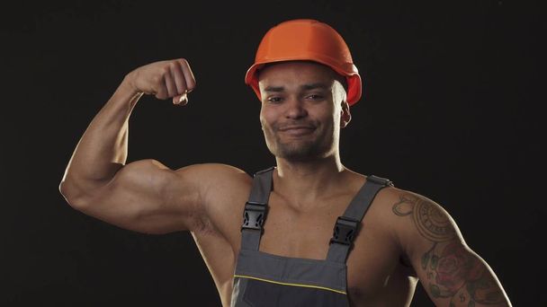 Muscular ripped sexy African male builder in workwear and hardhat flexing muscles - Foto, Bild
